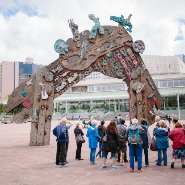 People in front of Selwyn Muru's Waharoa sculpture in Aotea Square, Auckland's city centre, with the Aotea Centre in the background. Image: Sacha Stejko.