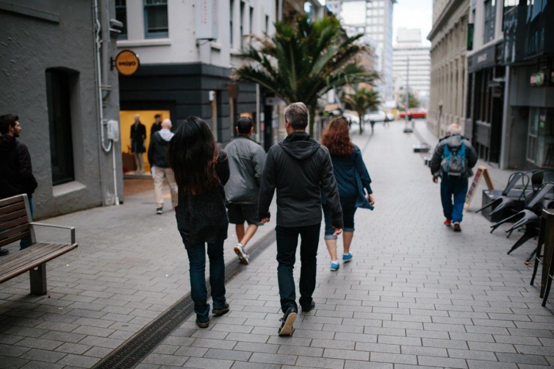 People walking in the O'Connell Street shared space in Auckland's city centre, with a Nikau palm and Mojo coffee sign in the background. Image: Sacha Stejko.