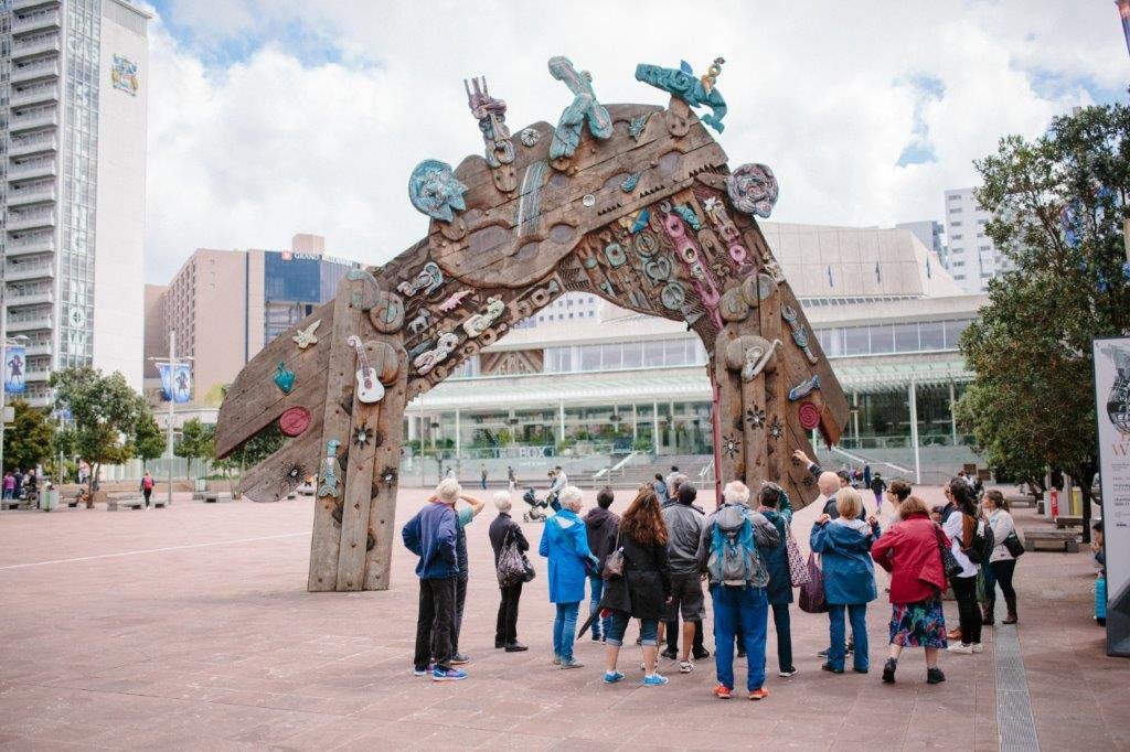 People in front of Selwyn Muru's Waharoa sculpture in Aotea Square, Auckland's city centre, with the Aotea Centre in the background. Image: Sacha Stejko.
